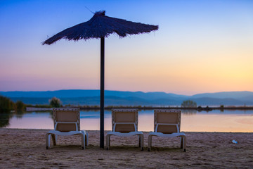 sunbeds together with sun umbrella on the beach in a sunset