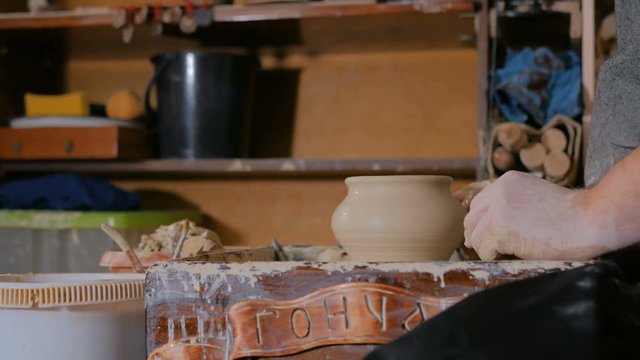 Professional male potter shaping and carving pot with special tool in pottery workshop, studio. Crafting, artwork and handmade concept