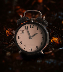Vintage alarm clock buried underneath colorful fallen autumn leaves with shallow depth of field. Daylight savings time concept with clock hands at almost 2 am.