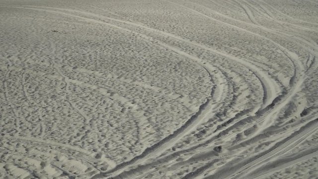 Tire tracks in deep, fine textured beach sand leading from foreground to background.  Slow pan.