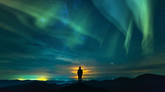 The man standing on the rock on the starry sky with a northern light background