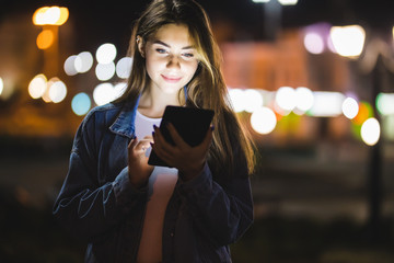 Beautiful young woman using tablet in the city at night bokeh