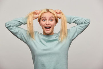 Lovely young blonde girl with long hair surprises, grimacing on camera, has fun jokes, rejoices,...
