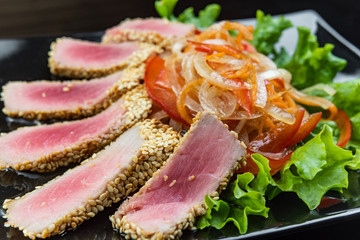 Close Up Still Life of Roasted Tuna Steaks Crusted with Herbs and Sesame Seeds on Dark Gray Surface