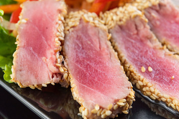 Close Up Still Life of Roasted Tuna Steaks Crusted with Herbs and Sesame Seeds on Dark Gray Surface