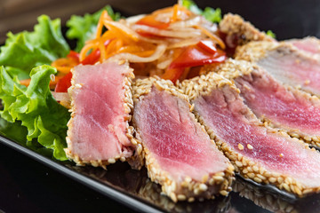 Fototapeta na wymiar Close Up Still Life of Roasted Tuna Steaks Crusted with Herbs and Sesame Seeds on Dark Gray Surface