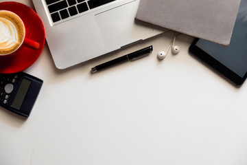 Office supplies are tablet, pen, computer, notebook, mobile phone and red coffee mug placed at an office desk and have a white background.
