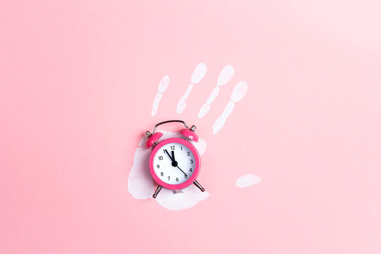 Pink alarm clock with white palm print on pink background. Top view, flat lay.