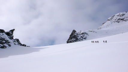 a group of backcountry skiers hike and climb to a remote moutain peak in Switzerland
