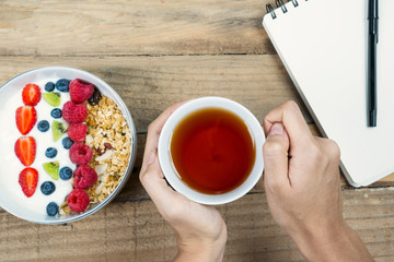 Woman hand with tea and yogurt on desk