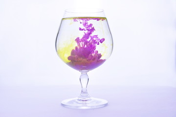 Yellow and violet paints fall in a wineglass with water