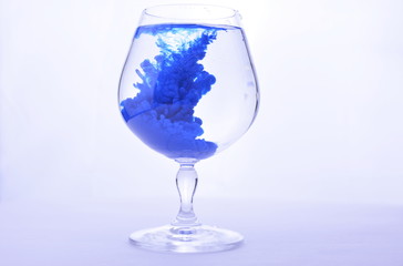 Blue paint in water in a crystal glass on a white background