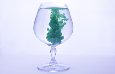 green paint in water in a crystal glass on a white background