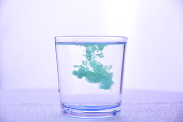 Glass with water on a white background with green paint