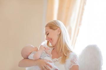 Beautiful mother and her baby son wearing angel costumes. Cheerful moment, loving family.