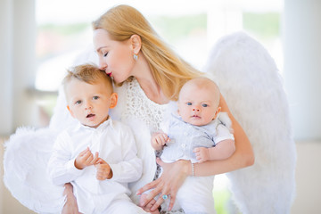 Beautiful mother with her toddler and newborn sons wearing angel costumes. Cheerful moment, loving family.