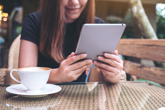 Closeup image of an asian woman holding and using tablet pc in cafe