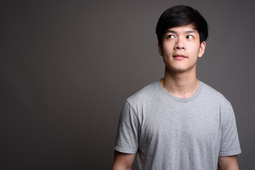 Young handsome Asian man thinking against gray background