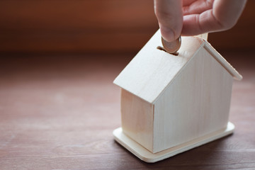 Hand putting euro money coin in wooden house on brown wood table background with copy space for text. Saving money to buy rent or build home in future concept.