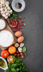 Italian food background, with tomatoes, basil, mushrooms, olives, olive oil, garlic, peppercorns, chilli, eggs, flour and oregano. Slate background.