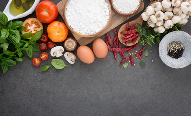 Italian food background, with tomatoes, basil, mushrooms, olives, olive oil, garlic, peppercorns, chilli, eggs, flour and oregano. Slate background.