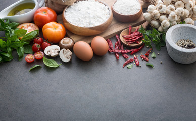 Obraz na płótnie Canvas Italian food background, with tomatoes, basil, mushrooms, olives, olive oil, garlic, peppercorns, chilli, eggs, flour and oregano. Slate background.