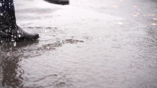 a girl in black leather boots walks in the autumn puddle during the rain in slow motion