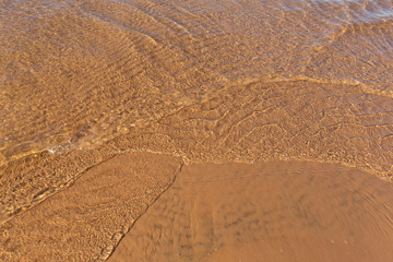 Beautiful sunlit small waves of shallow clear water on the smooth sand