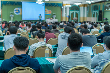 Rear view of Audience listening the speakers present the slide on the stage in the conference hall or seminar meeting, business and education concept