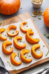 Baked pumpkin slices with thyme on a wooden board over grey table. Seasonal food vegetarian recipe.
