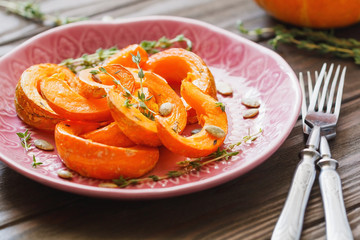 Baked pumpkin slices with thyme on a wooden board over grey table. Seasonal food vegetarian recipe.