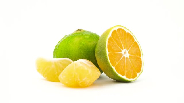 One whole and one half of a green tangerine fruits with water drops. Green mandarin slices rotating. Isolated on the white background. Close-up. Macro.