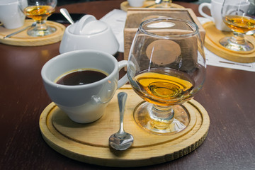 a cup of aromatic coffee and a glass of brandy on a wooden tray on a table in a restaurant