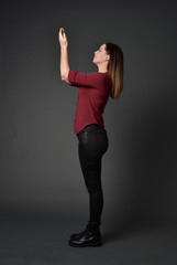 full length portrait of brunette girl wearing  red shirt and leather pants. standing pose , on grey studio background.