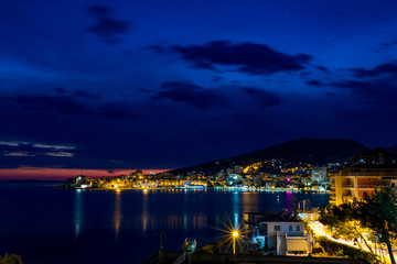 Obraz premium Long exposure night landscape photo, cityscape at the beautiful sea town of Saranda, Albania with star effect of the city lights and sea water reflections