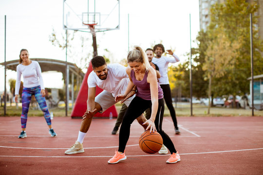 Group of multiracial young people   playing basketball outdoors