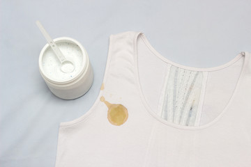 A spot on a white T-shirt, next to it is a container with a stain remover, close-up, bleach