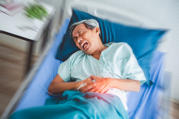 Old asian patient suffering from stomach ache, painful  lying on patient bed in hospital