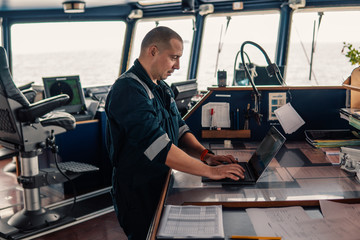 Marine navigational officer or technician is using laptop or notebook at sea. Job at sea