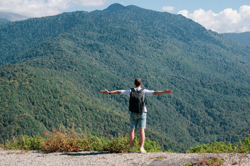 A young man enjoys a view of the mountains and stands on the edge of a cliff