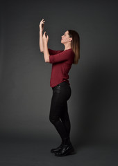 full length portrait of brunette girl wearing  red shirt and leather pants. standing pose , on grey studio background.