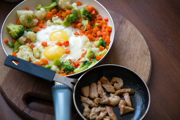 Scrambled eggs with broccoli and carrots. Slices of fried meat in a frying pan