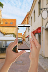 Naklejka premium A tourist is taking a photo of empty european street with cafe in the old town in Vilnius on a mobile phone