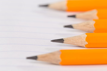 sharpened pencils lying on a notebook sheet in a strip