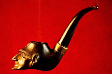 Smoking pipe-a device for ritual tobacco Smoking.  Pipe Smoking tobacco cherry with vintage carved ornament profile Mephistopheles on a bright red background.