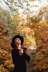 woman in dress and hat on background of autumn foliage