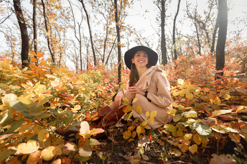 woman in dress and hat on background of autumn foliage