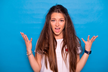 Cute brunette woman with long hair posing in white t-shirt on a blue background. Emotional portrait. She tries to tear her hair