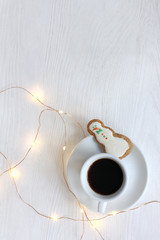 Happy Christmas drink/ small cup of black coffee with ginger cookies in the shape jolly snowman with festive garland on the table top view