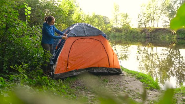 Woman is putting a tourist tent on the river bank